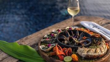 A seafood platter with mussels, oysters, and a fish on a wooden board, accompanied by a glass of white wine, set against a blurred background.