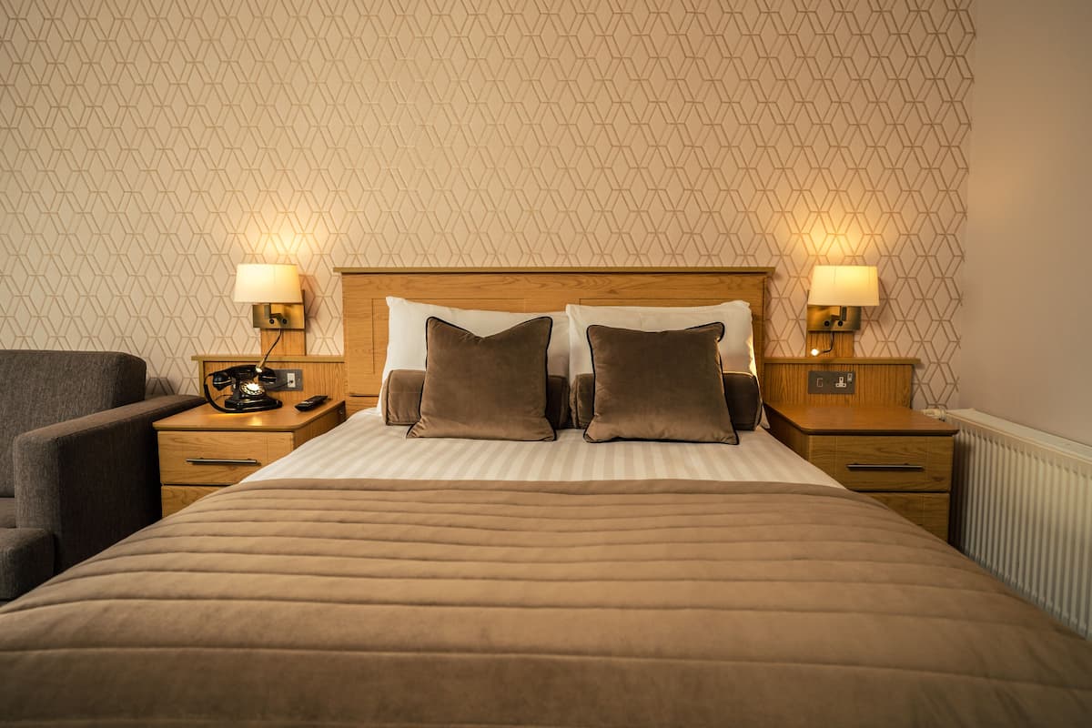 A hotel room with a large bed, two bedside tables with lamps, a chair, and a patterned wall.