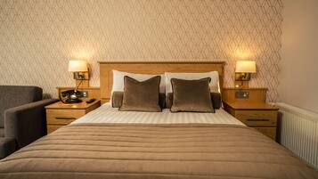 Habitación de hotel con una cama grande, dos mesitas de noche con lámparas, una silla y un papel tapiz estampado.