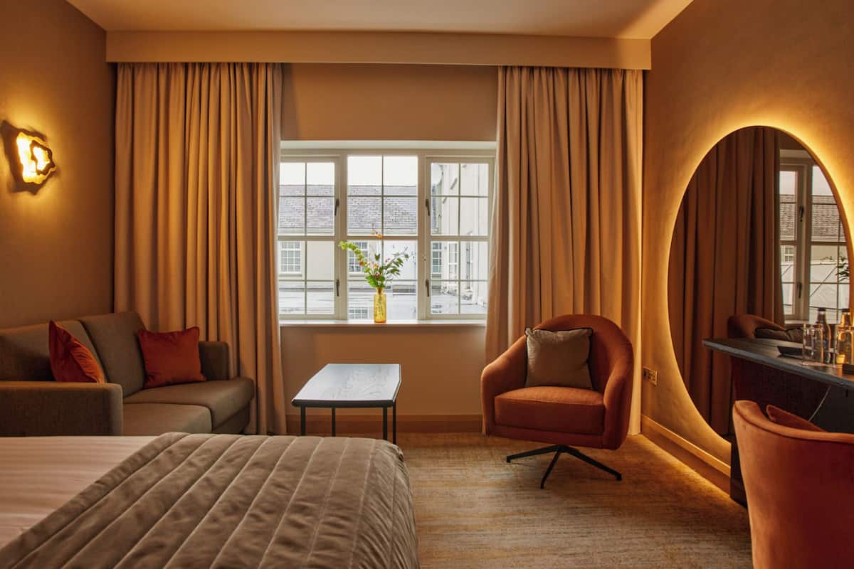 A hotel room with a bed, a sofa, a chair, a small table, and a window with curtains.