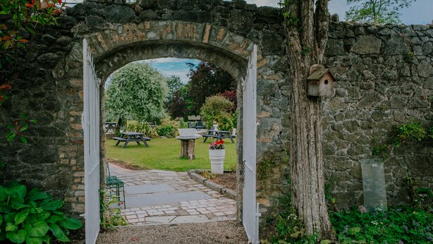 An archway leading to a garden with picnic tables and a birdhouse. - County Arms Birr (Birr)