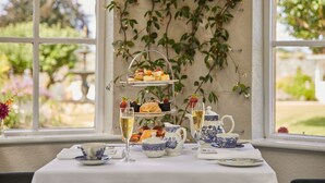 A three-tiered dessert stand with pastries and fruits, a teapot, cups, and a pitcher on a table by a window with a view of greenery. - County Arms Birr (Birr)