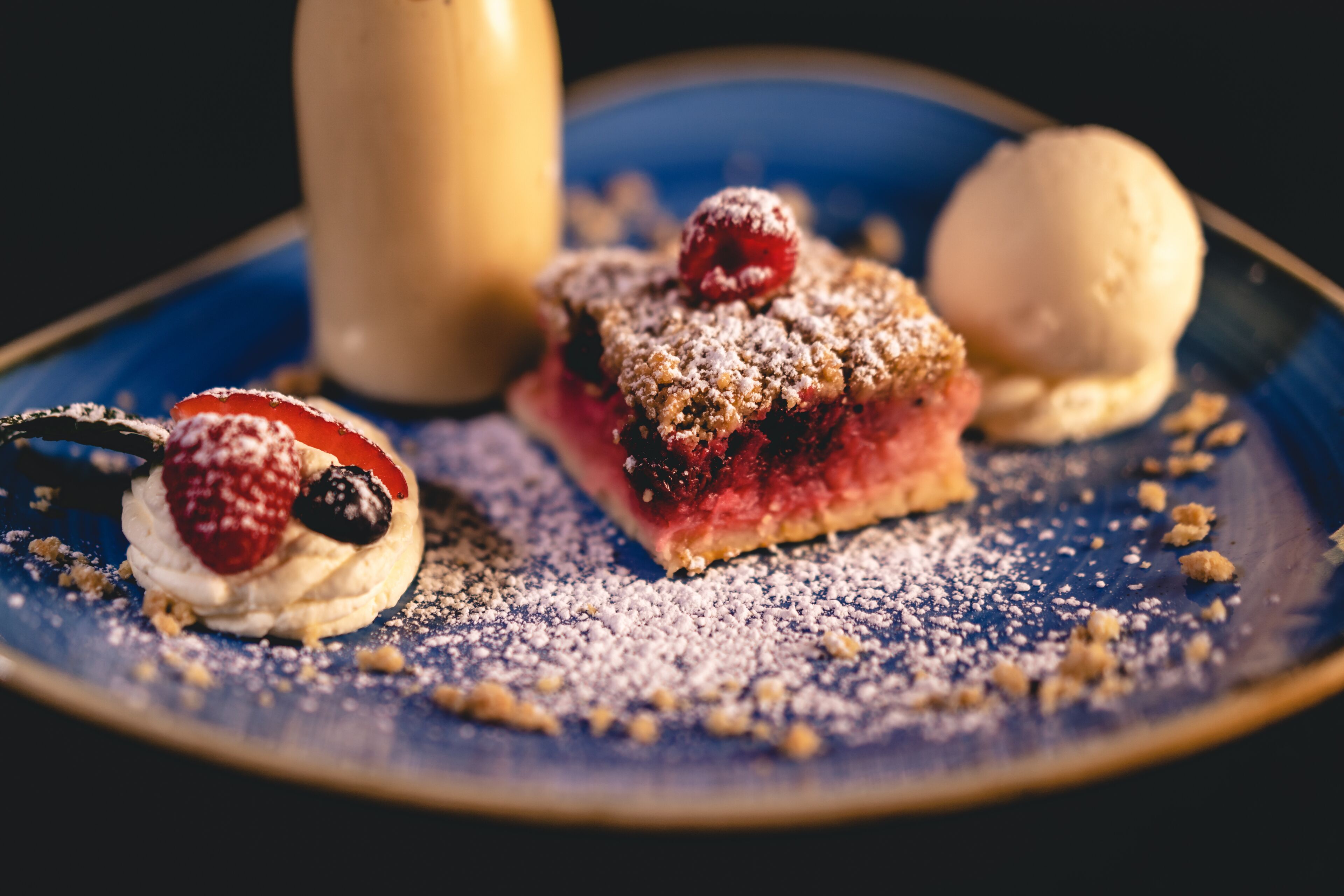 Un plat de postres amb una porció de pastís, una bola de gelat i un brioix farcit amb fruita.