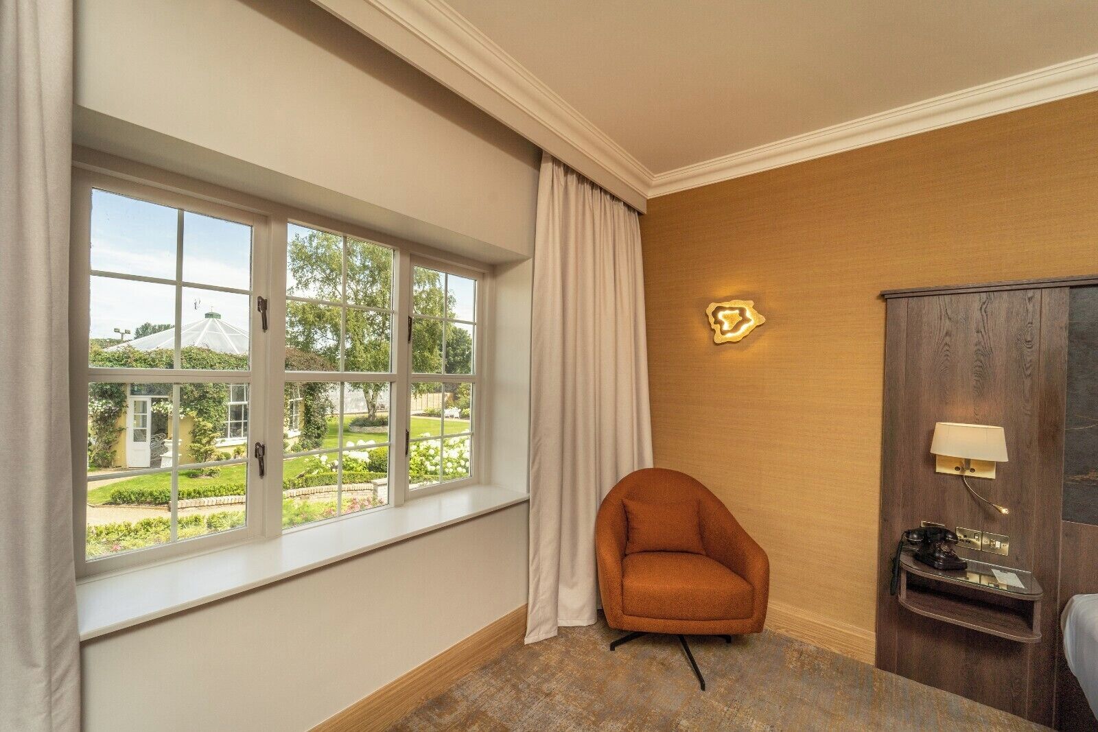 A room with a large window, a chair, a cabinet, and a lamp.