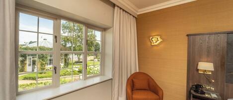 A room with a large window, a chair, a cabinet, and a lamp.