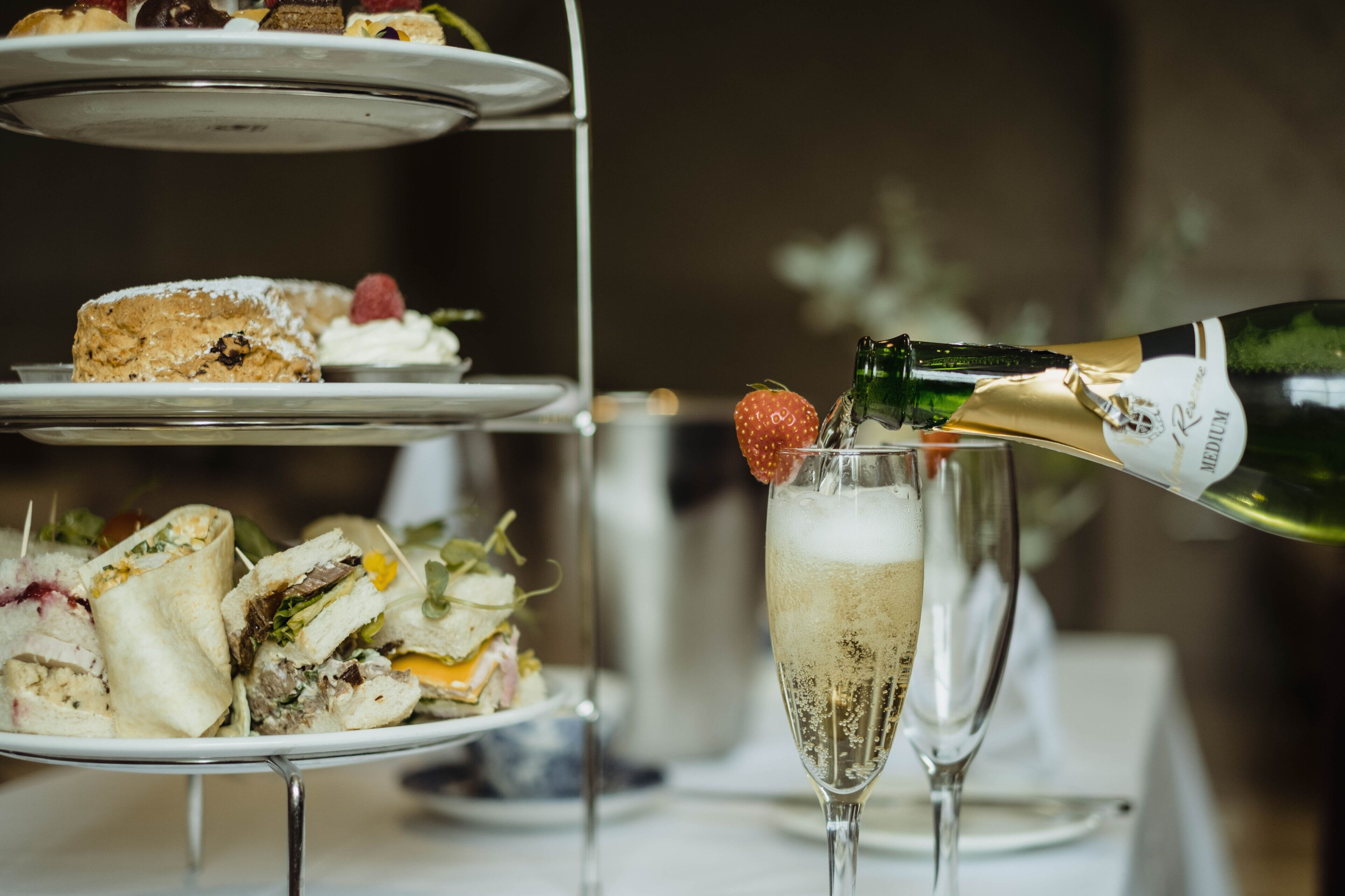 A multi-tiered dessert stand with various pastries and a bottle of champagne being poured into a glass.