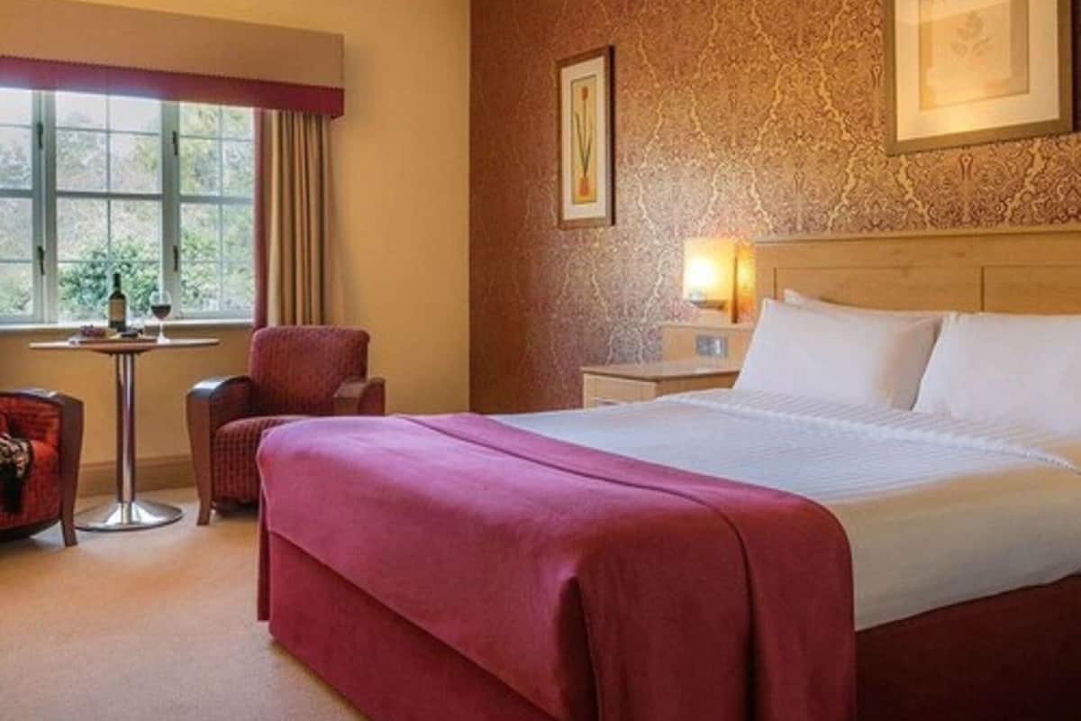 A hotel room with a bed, a chair, a small table, and a window.