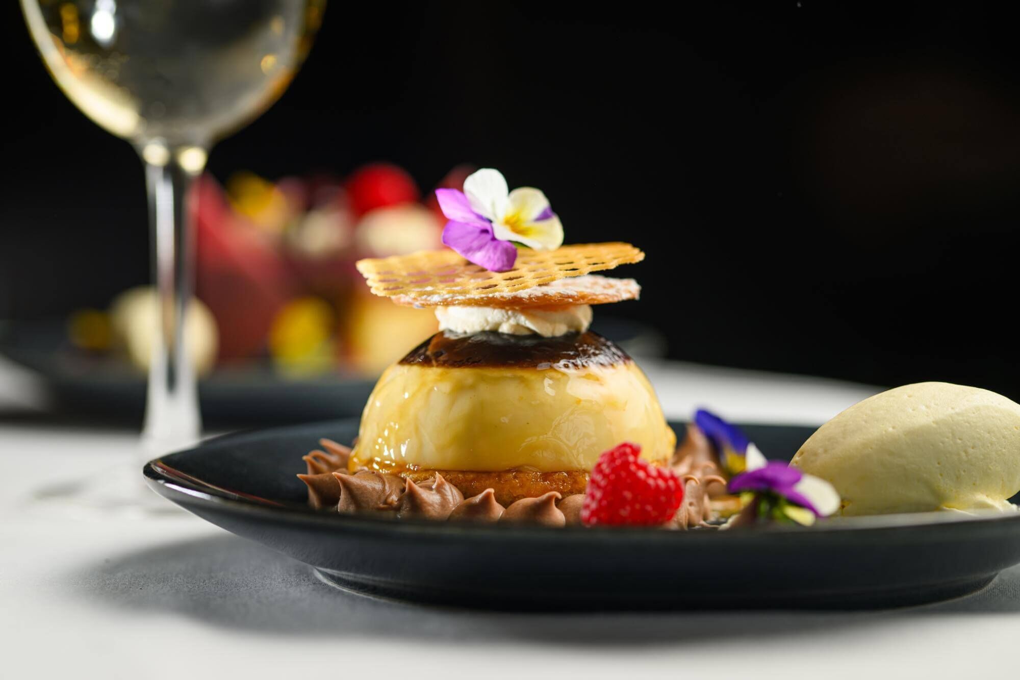 A dessert with a caramelized top, a wafer, and a flower on a plate.