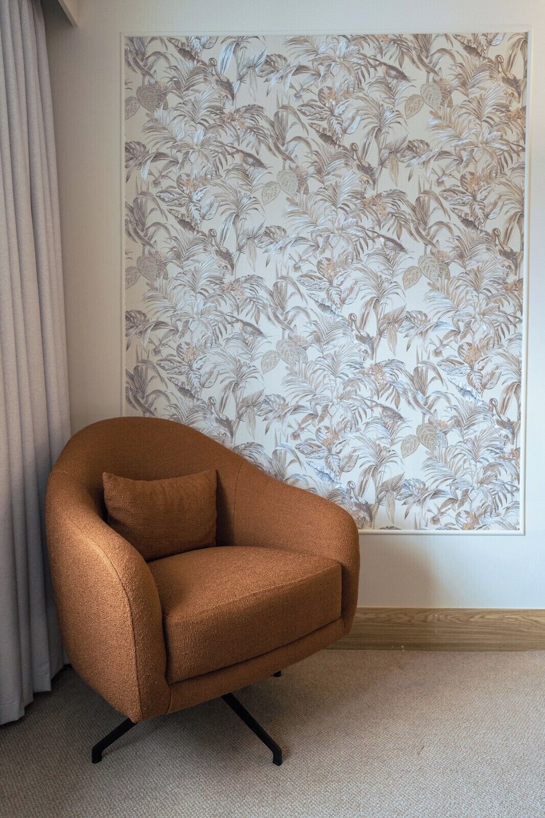 Una habitación con un papel tapiz floral grande, un sillón marrón y una alfombra de color claro.