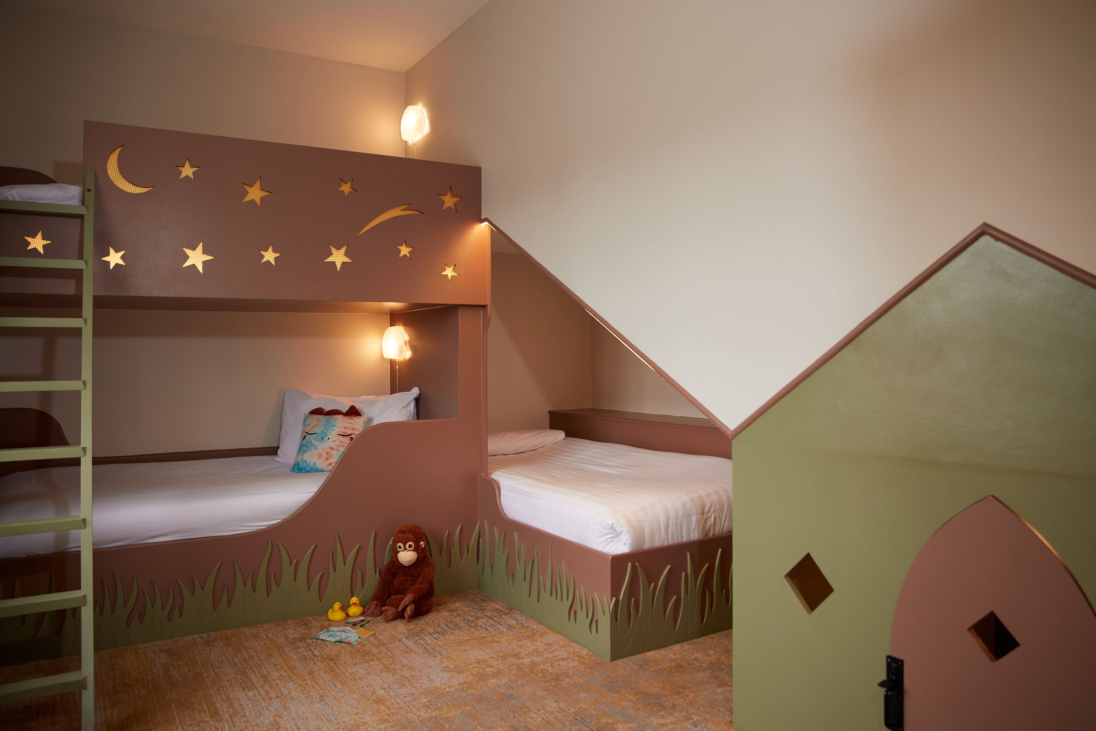 Habitación infantil con literas, un pequeño espacio de juegos y una puerta que parece una casa.