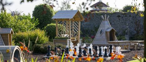 A garden with a chessboard, wooden play structures, and a stone wall.