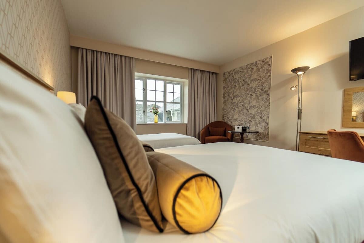 A hotel room with a large bed, a chair, a table with a lamp, and a window with curtains.