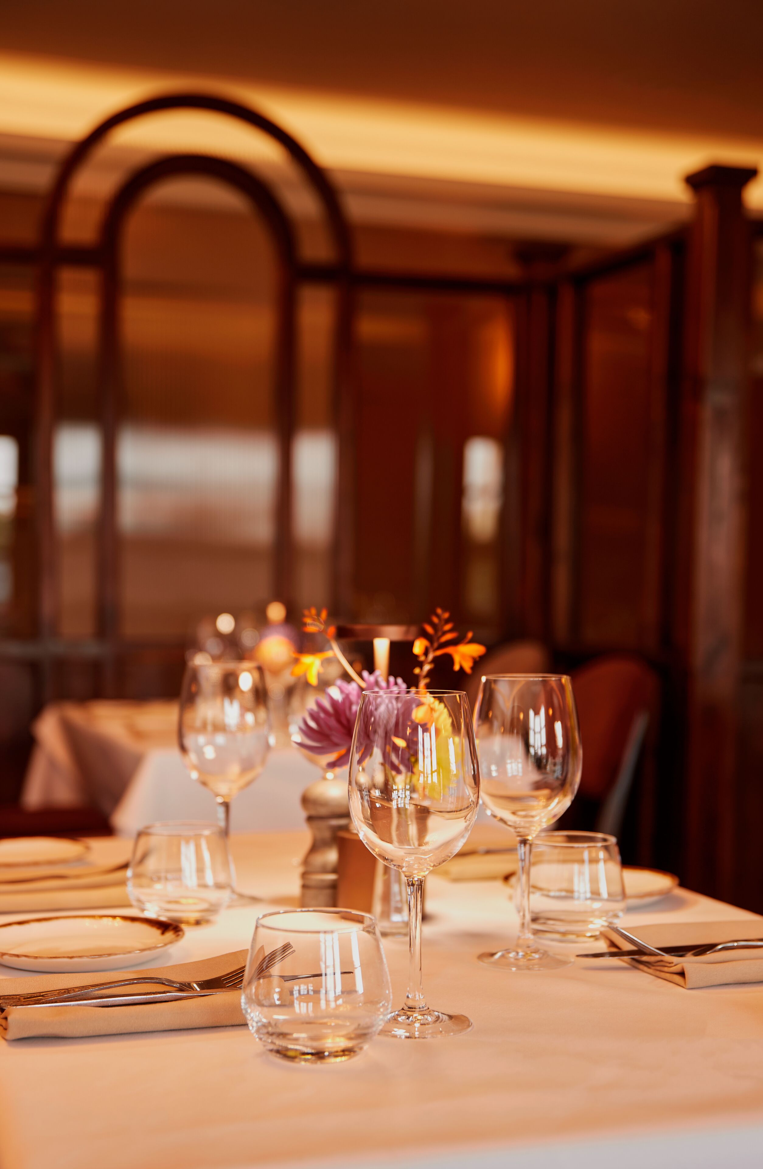 A dining table set with wine glasses, a vase with flowers, and cutlery.