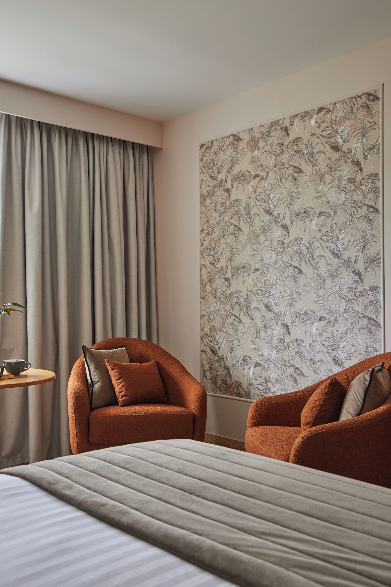Ein Hotelzimmer mit einem Bett, zwei Sessel, einem Beistelltisch und üppigem Blumenwallpaper.