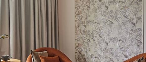 Ein Hotelzimmer mit einem Bett, zwei Sessel, einem Beistelltisch und üppigem Blumenwallpaper.