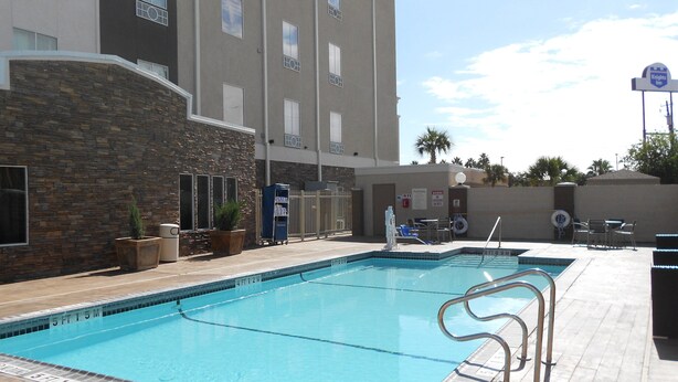 A swimming pool with a stone wall and a building in the background. - Holiday Inn Express and Suites Corpus Christi North by IHG (Corpus Christi)