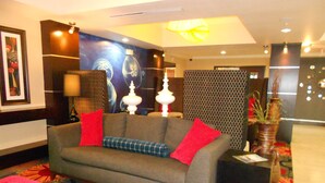 A modern lobby with a grey sofa, red cushions, a patterned rug, and a decorative vase. - Holiday Inn Express and Suites Corpus Christi North by IHG (Corpus Christi)