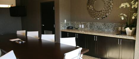 A modern conference room with a dark wooden table, white chairs, a granite countertop, and a decorative mirror on the wall.