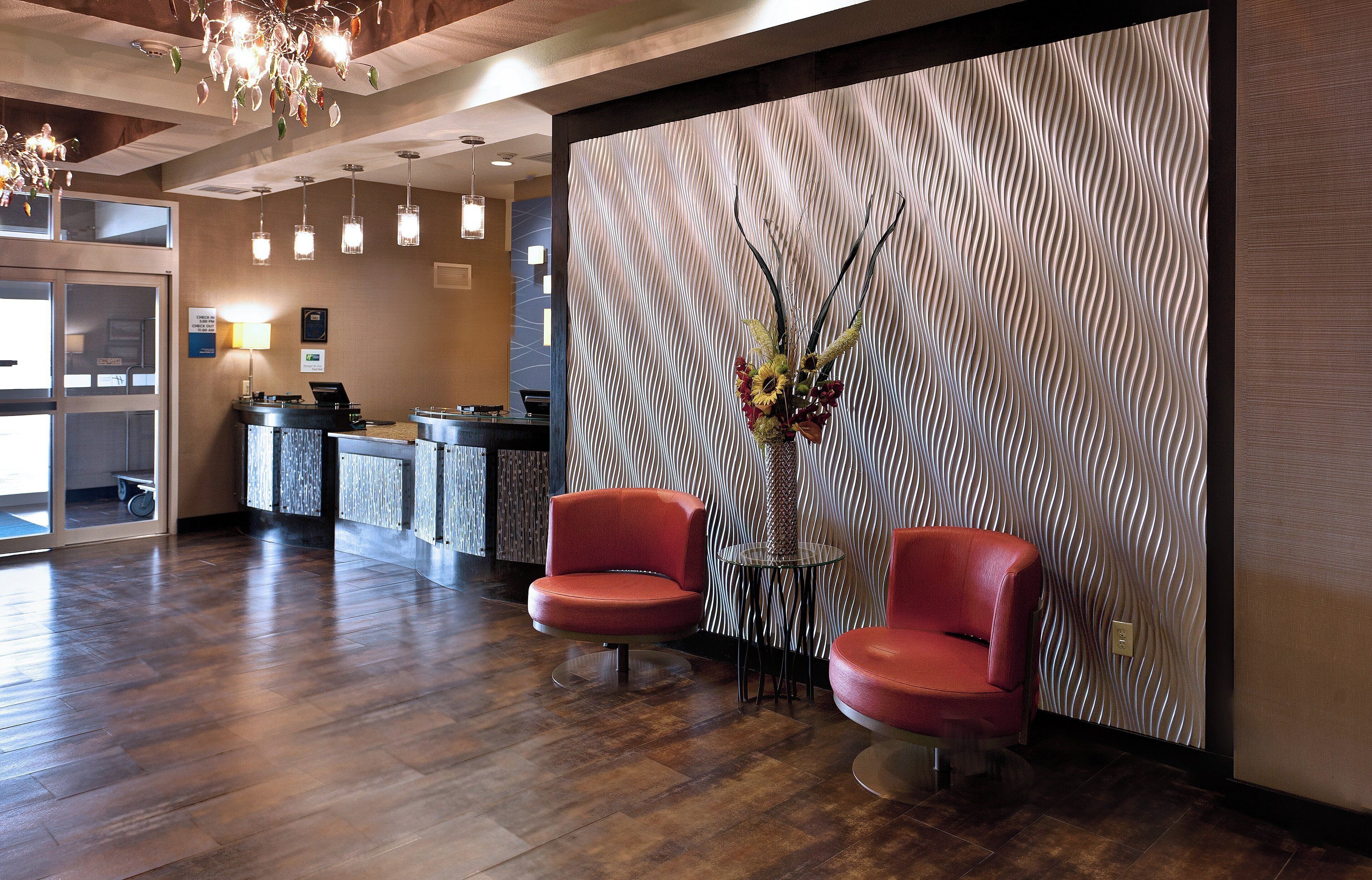 A reception area with a modern design, featuring a reception desk, two red chairs, a decorative wall, and a chandelier.