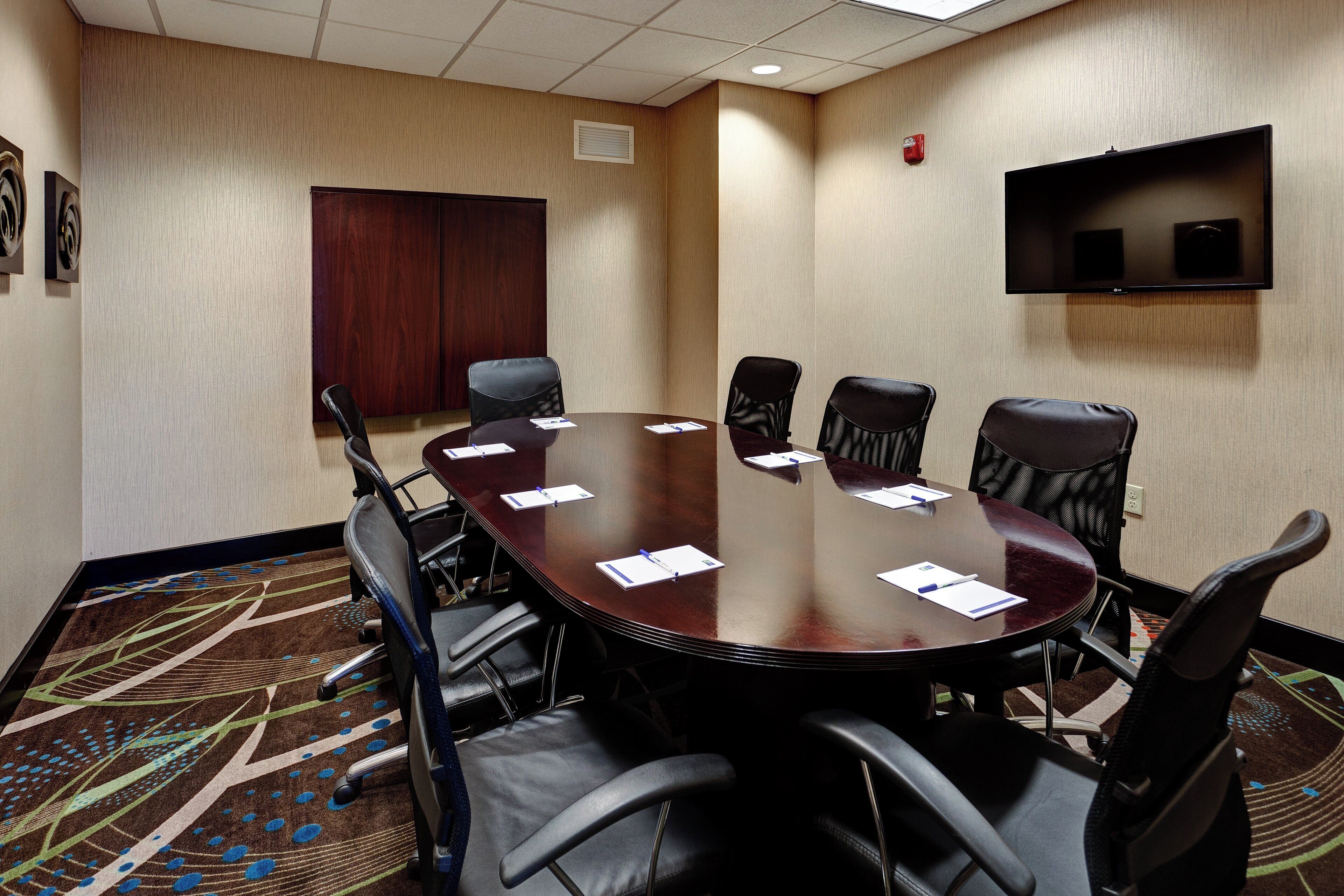 A conference room with a round table, black chairs, and a flat-screen TV mounted on the wall.
