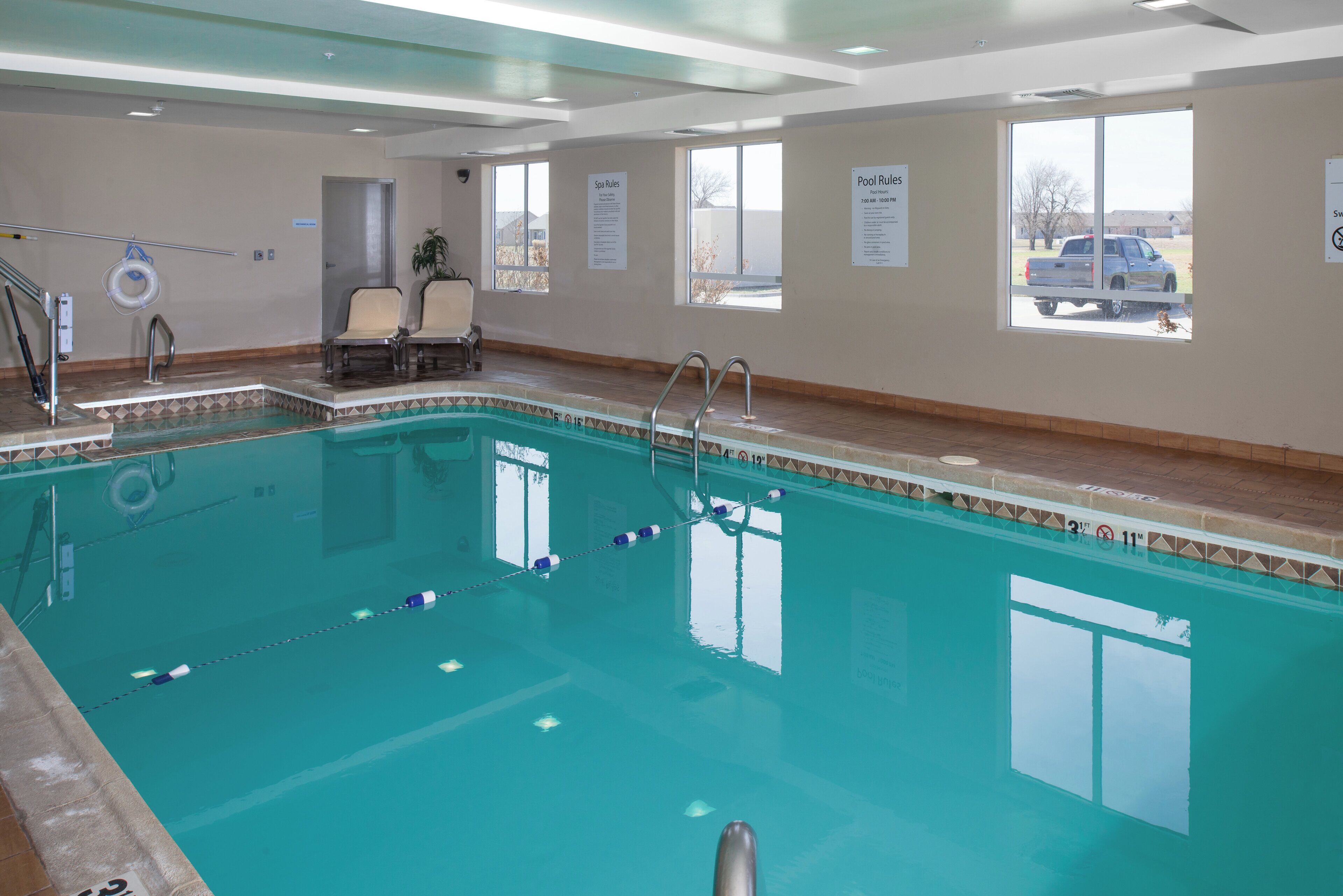 An indoor swimming pool with clear water, safety signs, and a view of the outside.