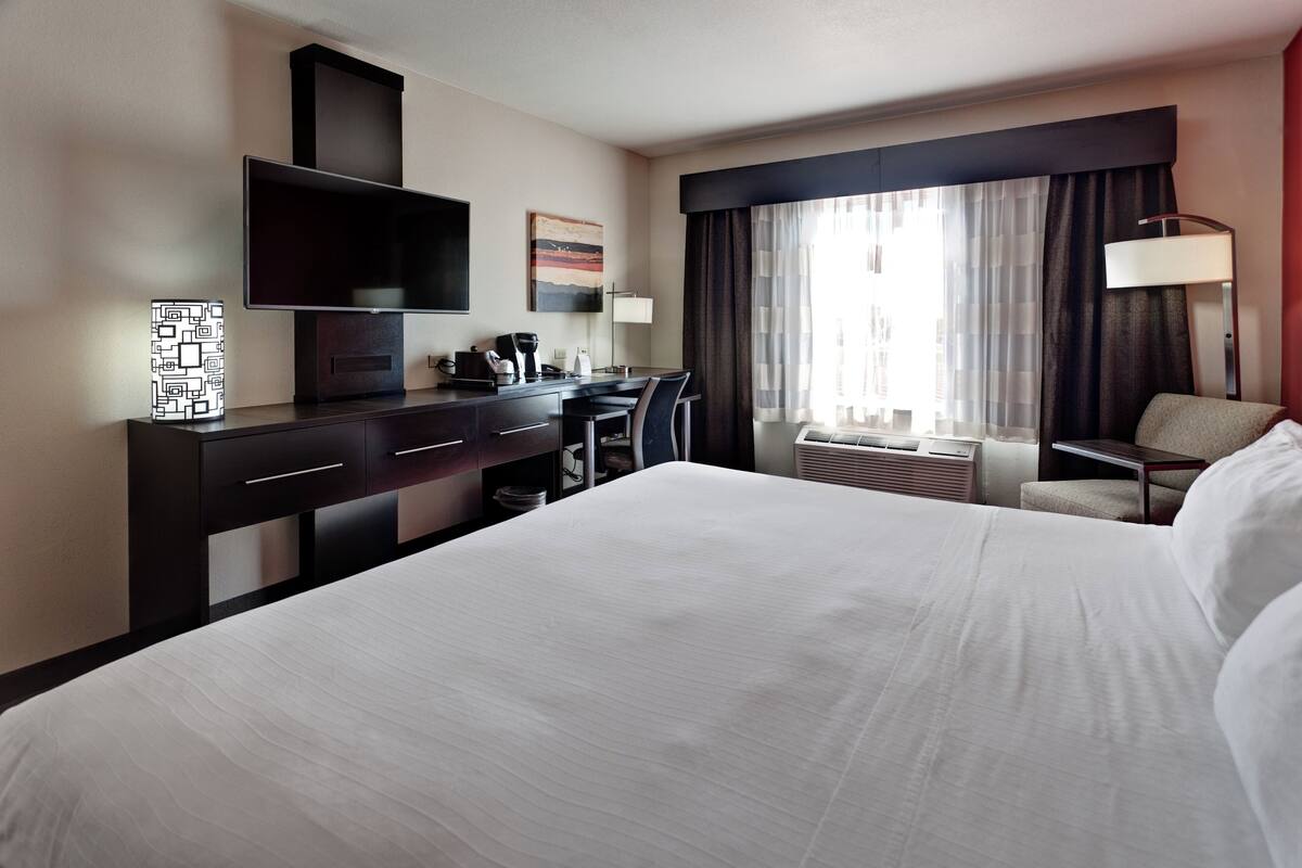 Une chambre d’hôtel avec un grand lit, un bureau doté d’un téléviseur à écran plat, une machine à café et une fenêtre avec des rideaux.