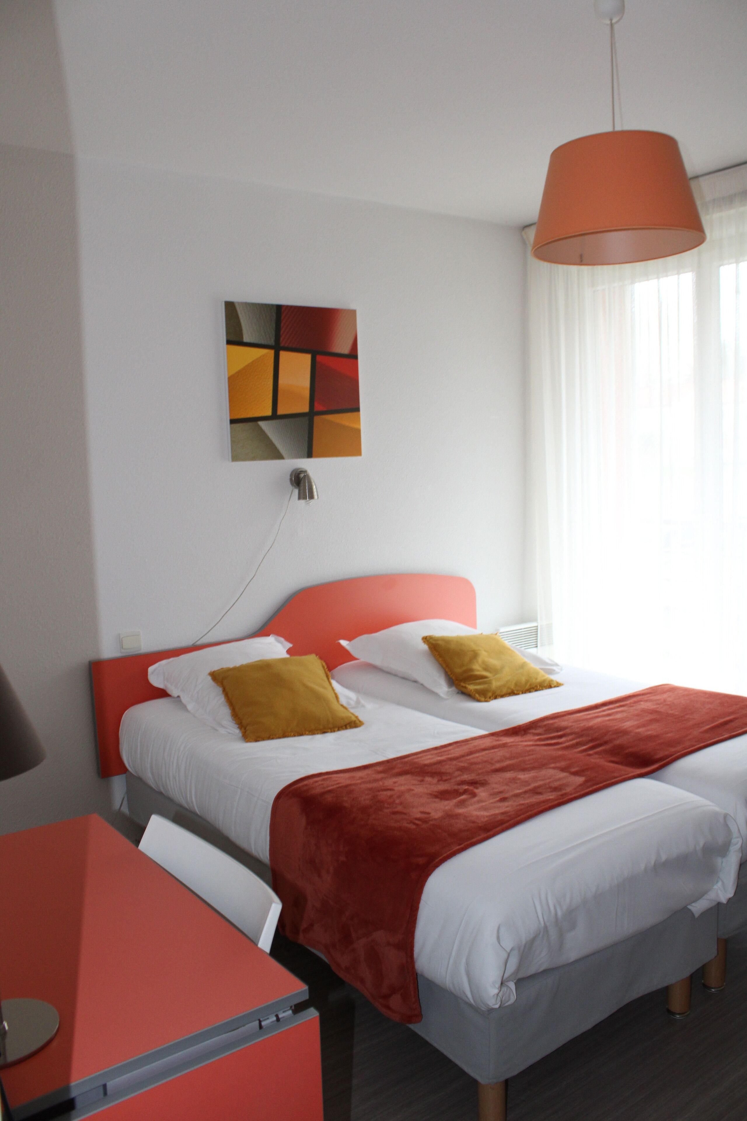 A hotel room with a bed, a desk, and a painting on the wall.