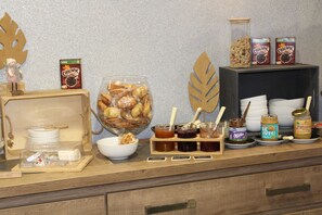 A buffet setup with various food items, including a large bowl of fruits, jars of spreads, and boxes of Chocapic.