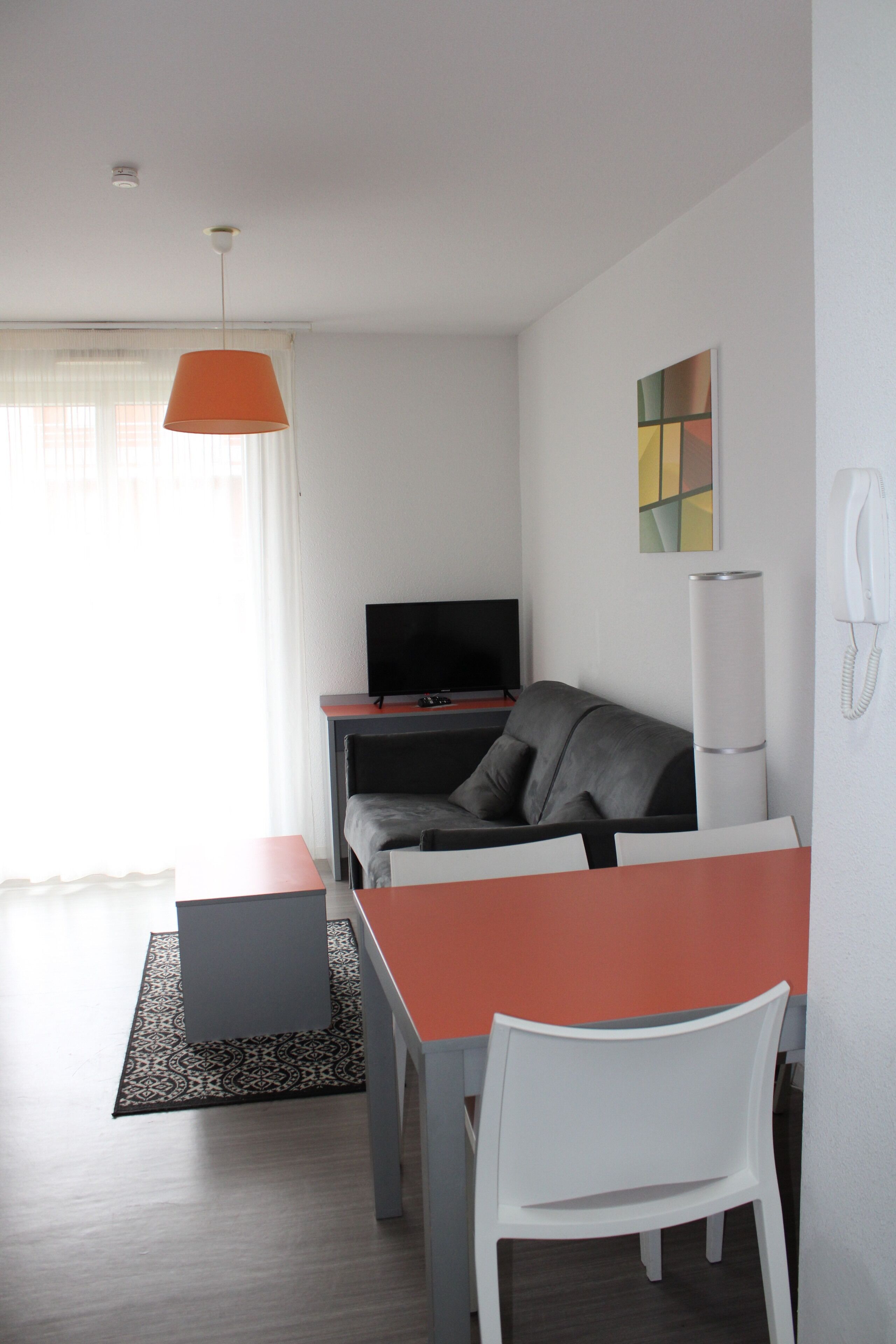 Un espacio habitable moderno y funcional con una mesa de comedor, un sofá, un televisor y un teléfono.