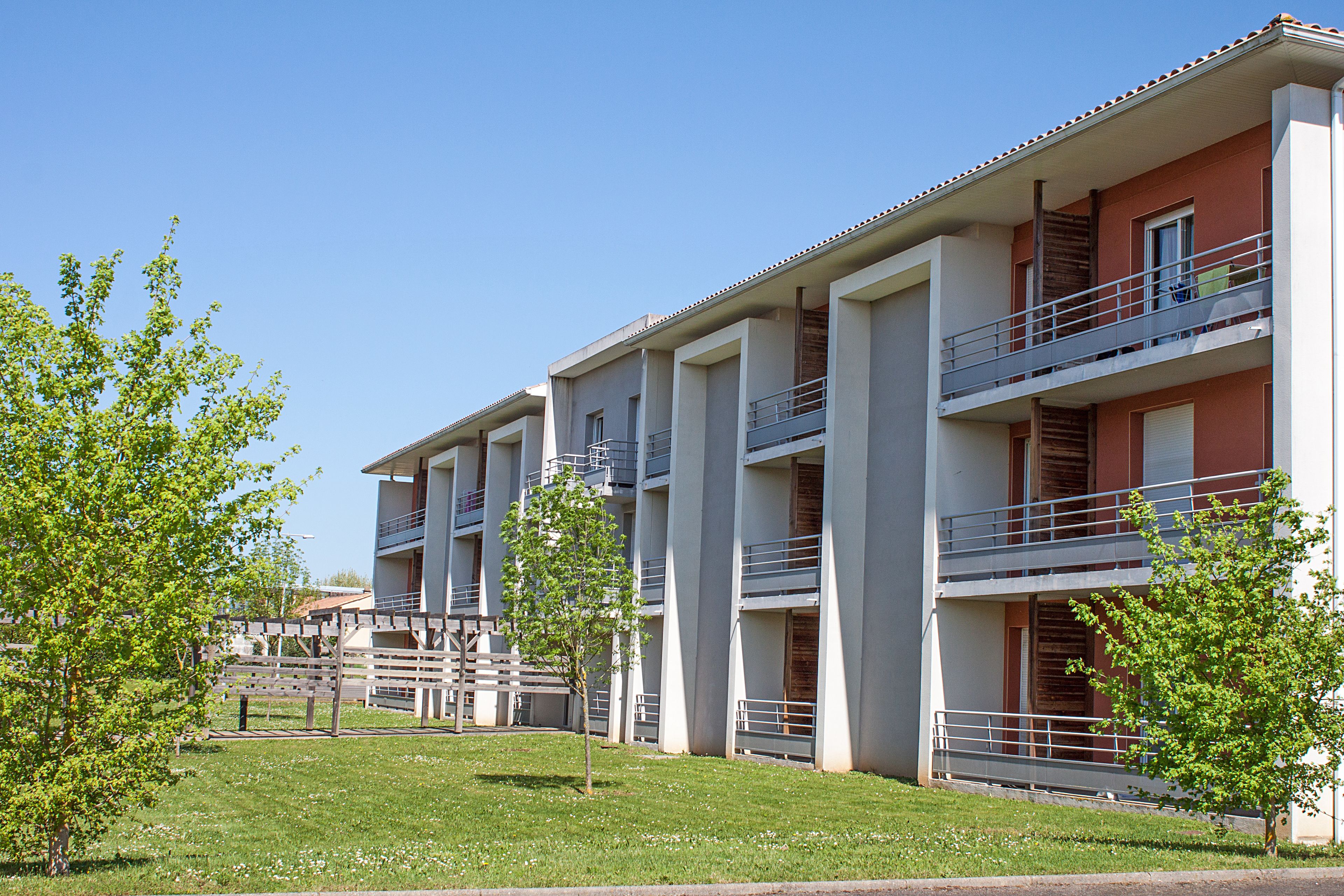 A multi-story building with balconies and a grassy area in front.