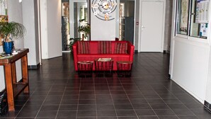 Un vestíbulo con un sofá rojo, una mesa de madera con una planta y una alfombra negra con el texto "Le City Lodge".