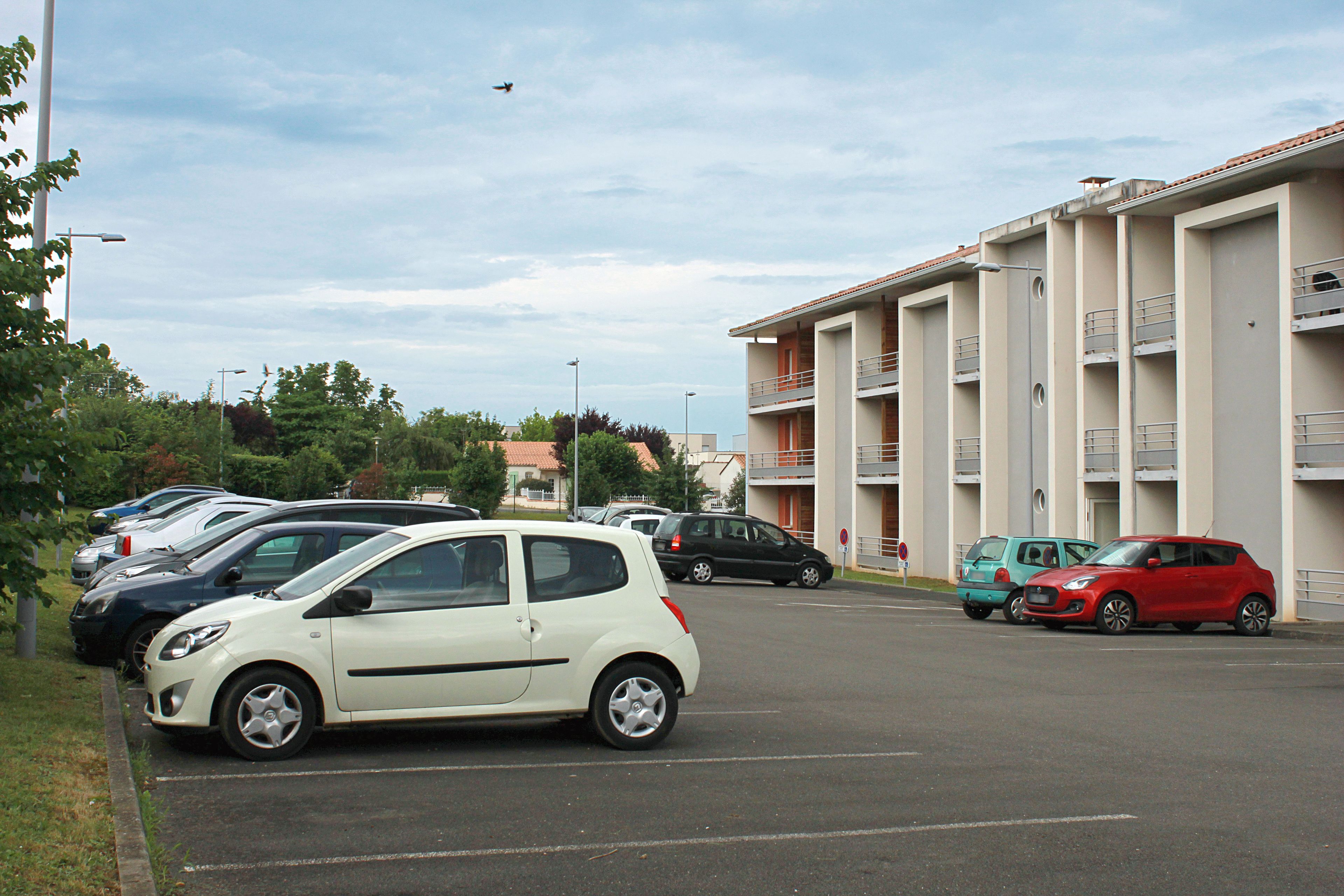 Un estacionamiento con varios autos estacionados frente a un edificio con balcones.