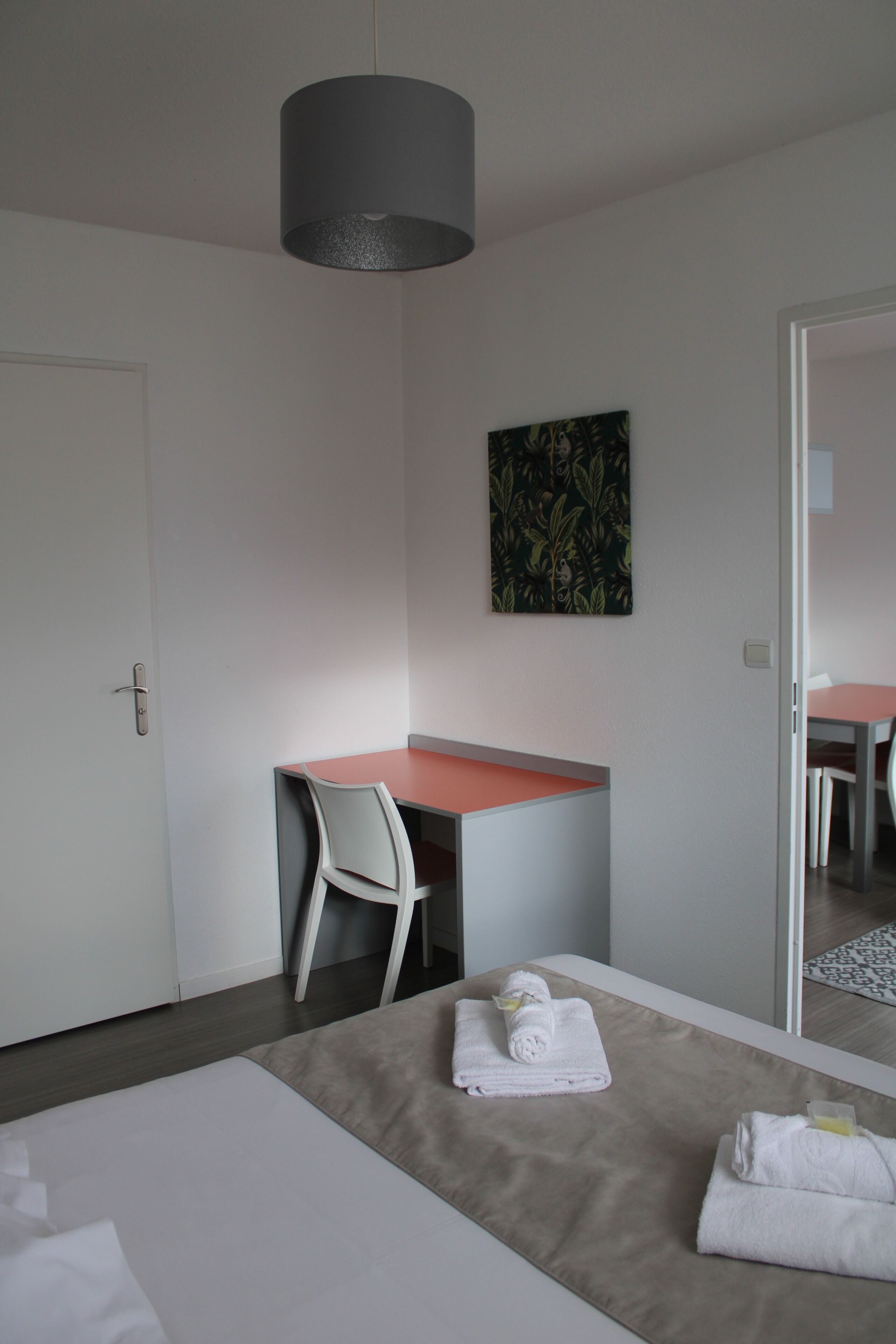 A modern hotel room with a bed, a desk, a chair, and a hanging light fixture.