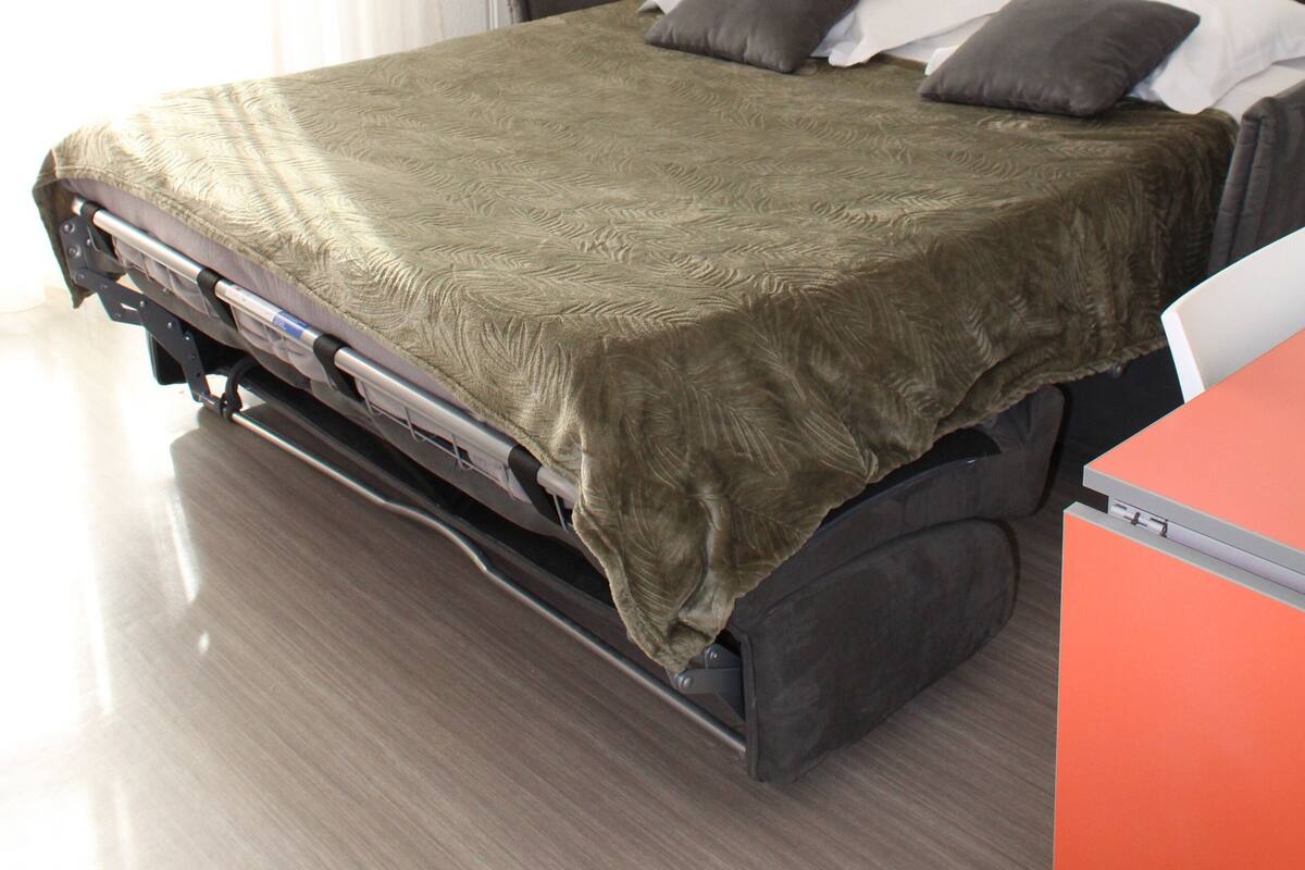 Een moderne hotelkamer met een bed, nachtkastje, lamp en een kunstwerk aan de muur.