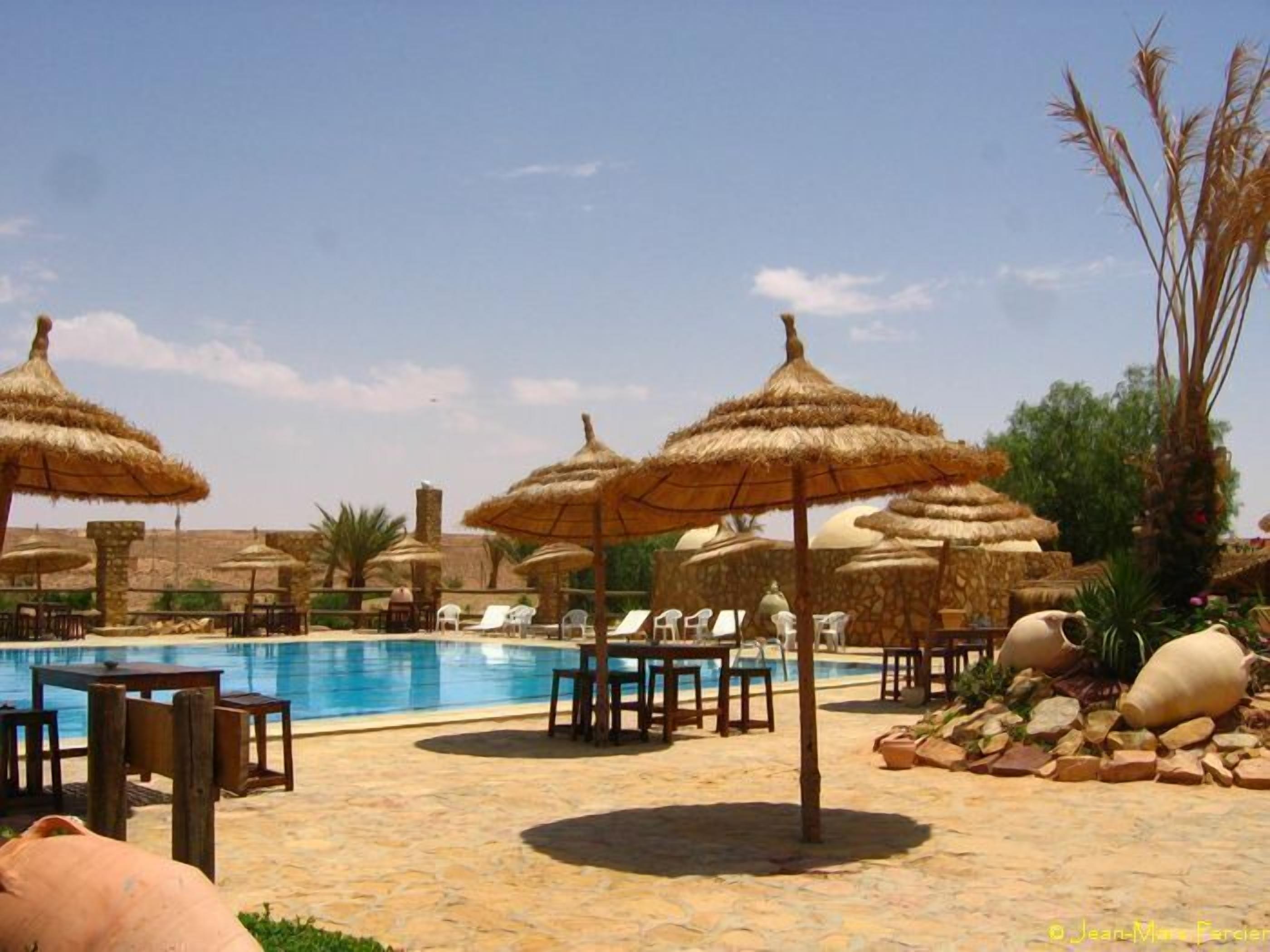 A pool area with thatched umbrellas, lounge chairs, and stone flooring.