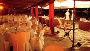 An indoor dining area with tables set for a meal, a chef at work, and a tented structure.