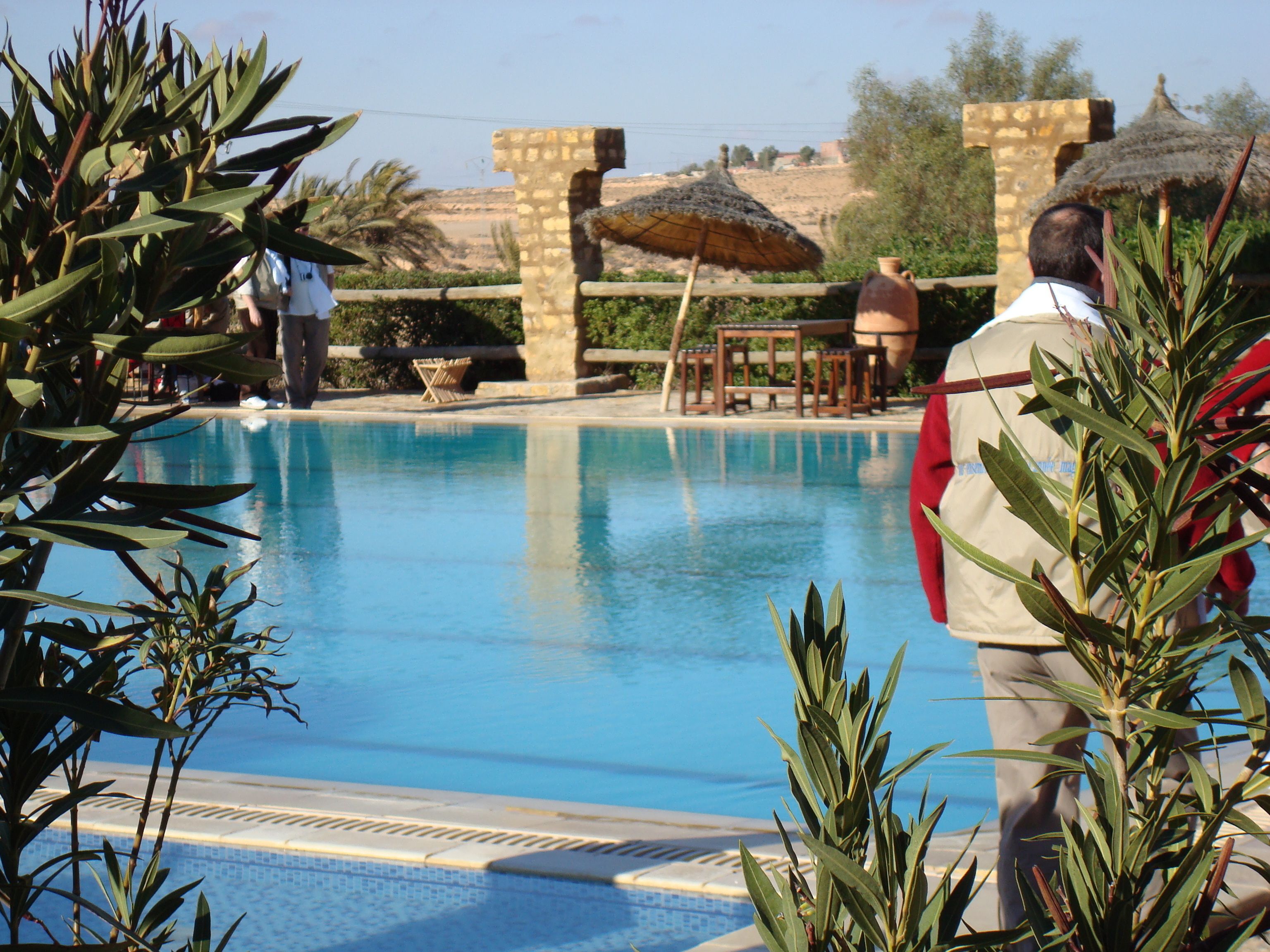 A swimming pool with a stone wall and a thatched umbrella.