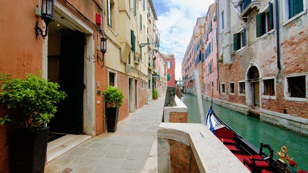 A narrow Venetian canal with buildings on either side, a gondola docked on the right, and a potted plant on the left. - Hotel Le Isole (Venice)