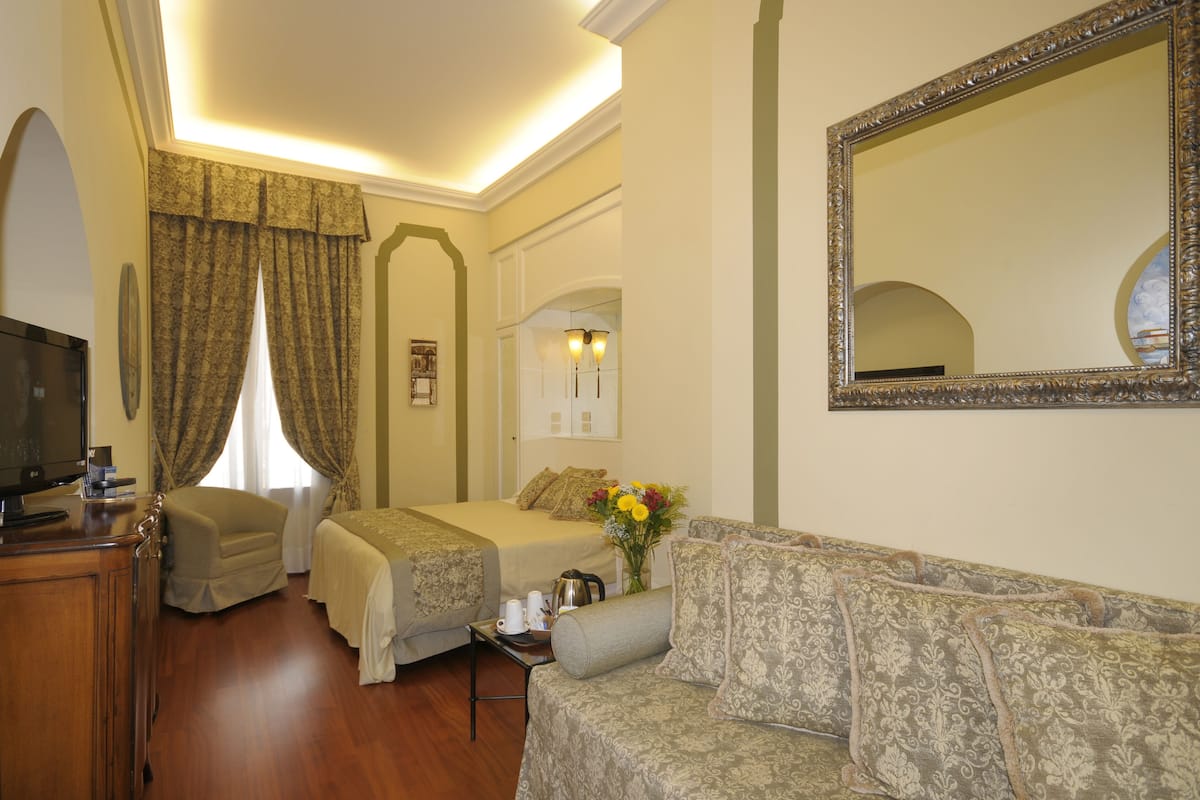 A hotel room with two beds, a sofa, a TV, and a mirror.