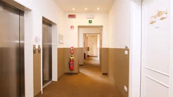 A hotel corridor with elevators, fire extinguishers, and a fire exit sign.