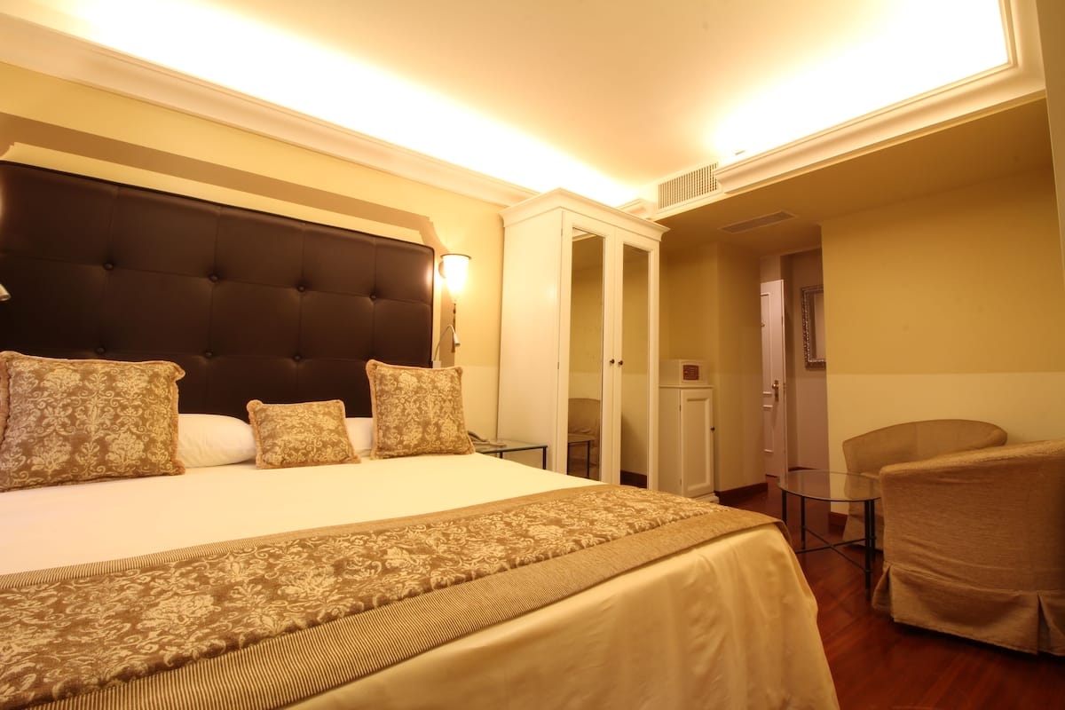 A hotel room with a large bed, a bedside table, a chair, and a wardrobe.