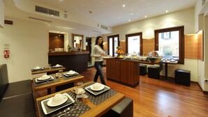 A hotel dining area with tables set for service, a kitchen in the background, and a person walking through the space. - Hotel Le Isole (Venice)