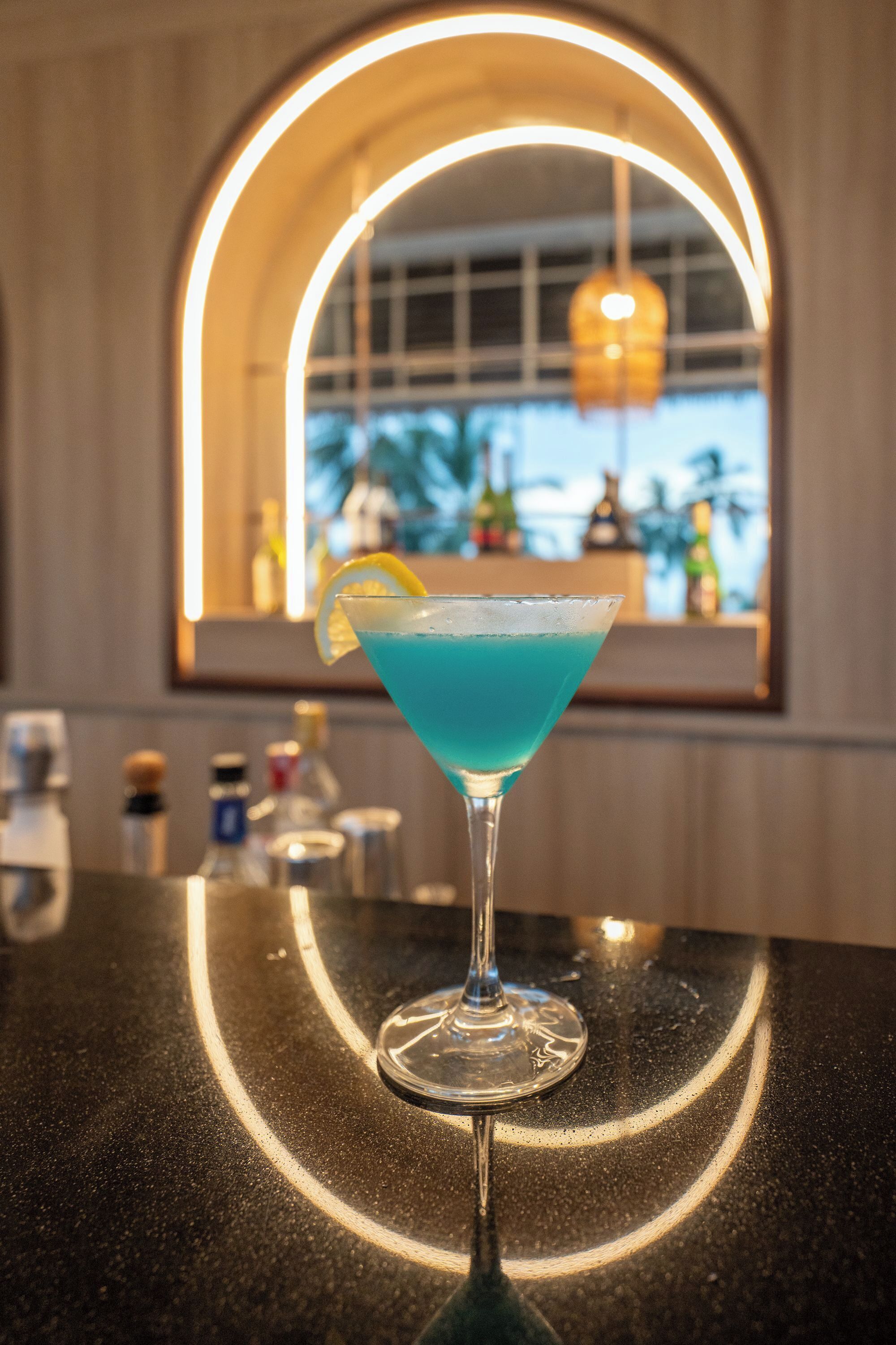 Un cocktail servi dans un verre à martini, agrémenté d’une tranche de citron, posé sur le comptoir d’un bar.