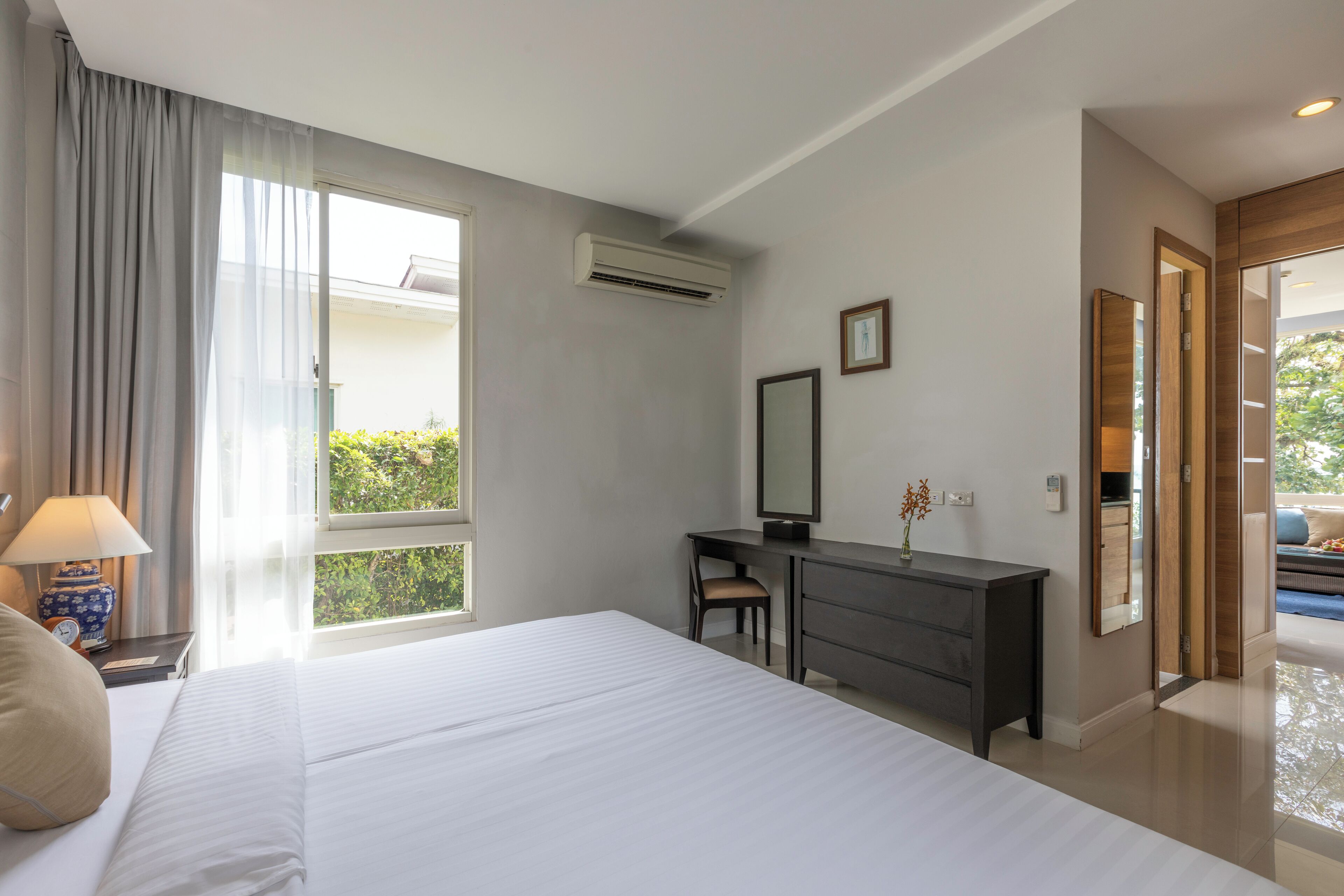 Habitación de hotel con una cama grande, un escritorio con silla, cómoda, espejo y ventana con cortinas.
