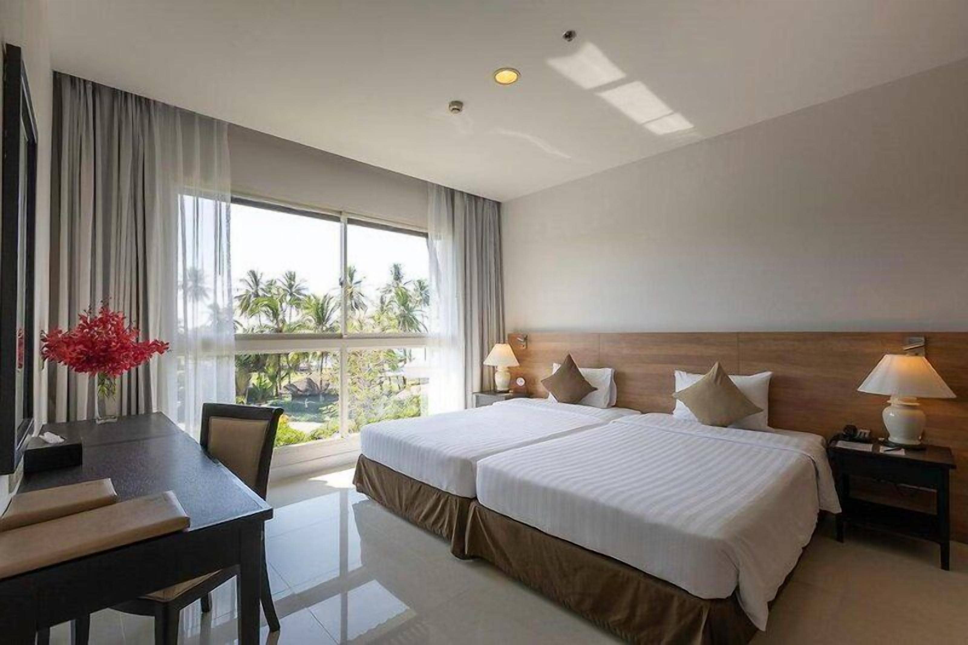 A hotel room with two beds, a desk, and a view of palm trees.