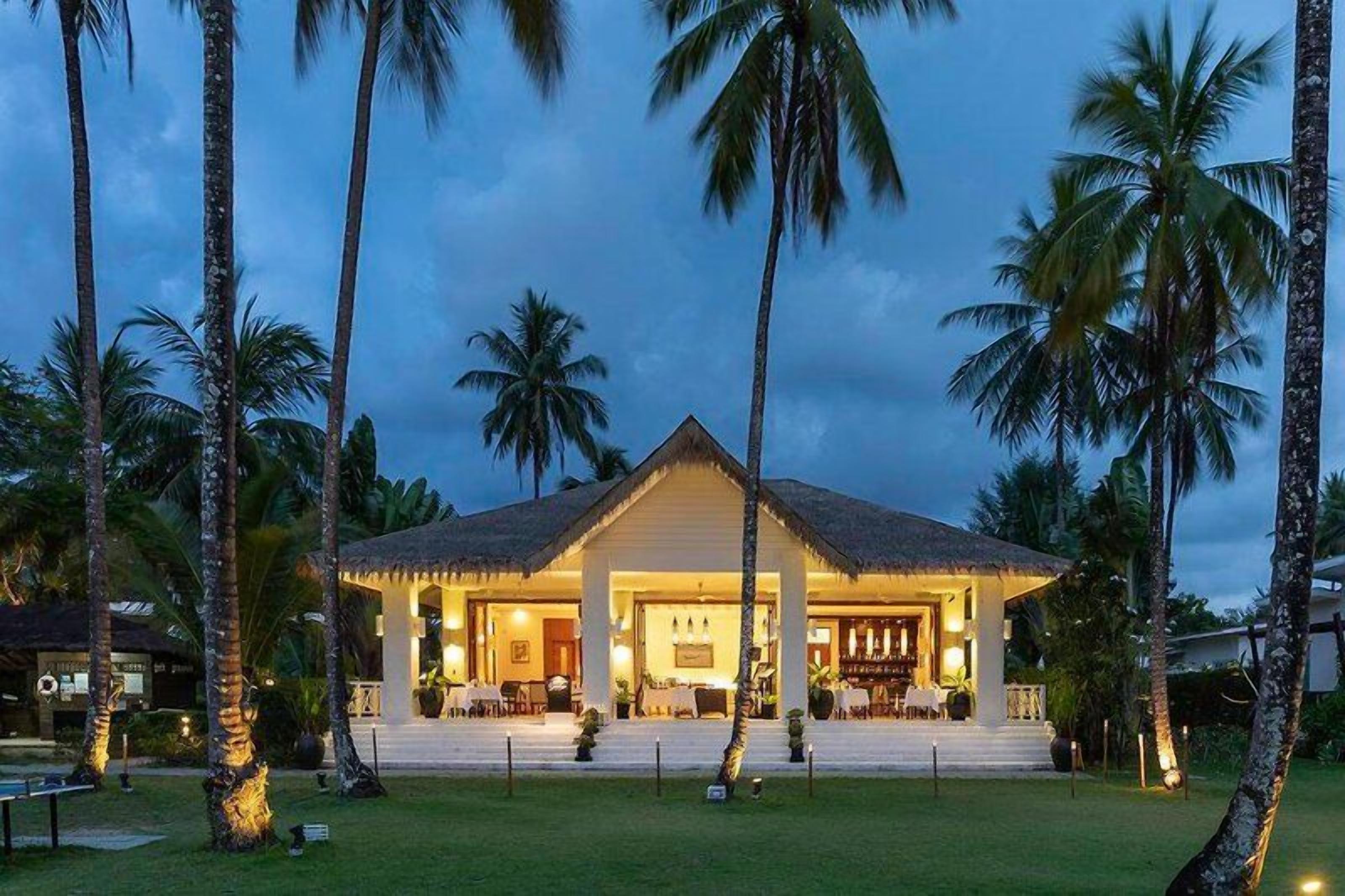 A two-story building with a central entrance, surrounded by palm trees, and a well-lit exterior.