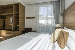 A hotel room with a large bed, wooden wardrobe, and a window with sheer curtains.