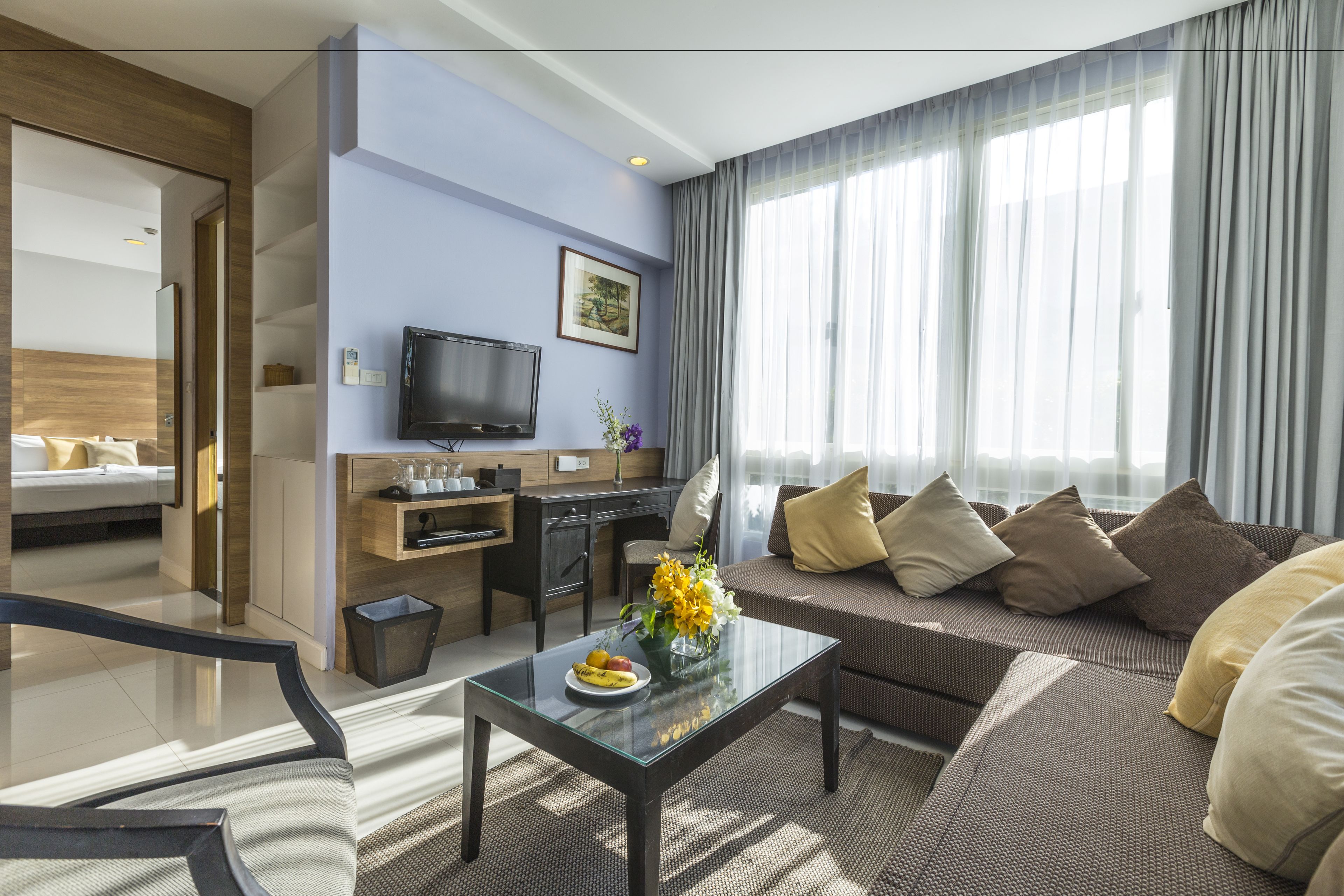 Una habitación de hotel moderna con un sofá, una mesita de centro con fruta, un televisor y un escritorio.