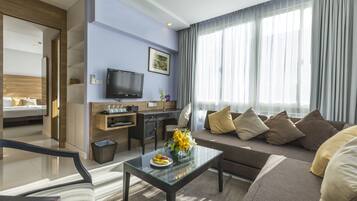 Una habitación de hotel moderna con un sofá, una mesita de centro con fruta, un televisor y un escritorio.