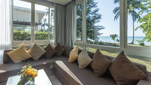 Un salon moderne avec un grand canapé, de nombreux coussins et une vue sur l’océan et les palmiers.